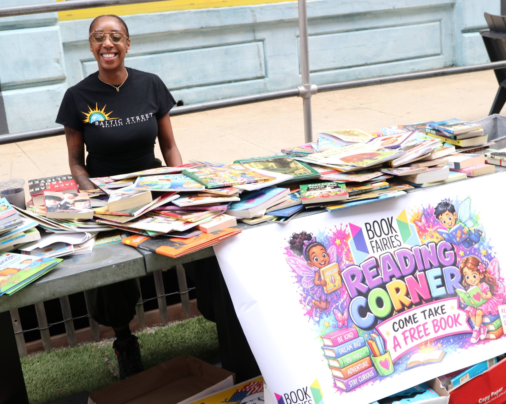 Person smiling behind a table of books at a community gathering
