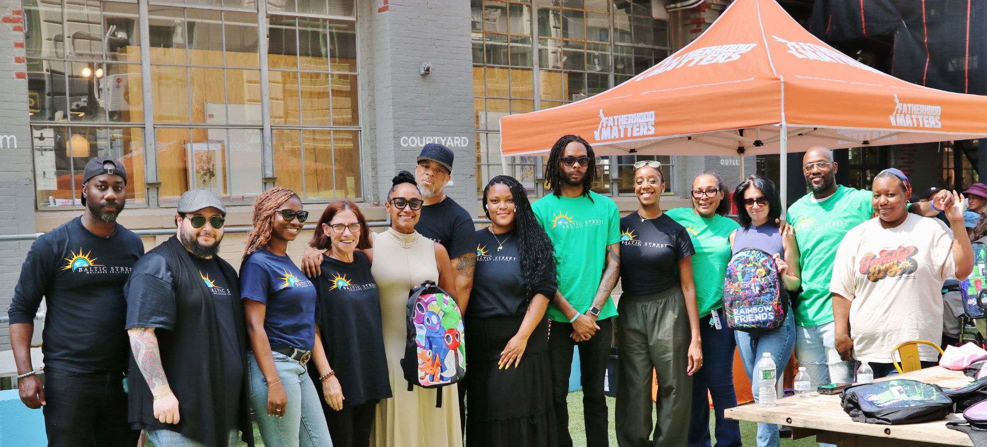 A large group of Baltic Street team members and partners outdoors under a Fatherhood Matters tent